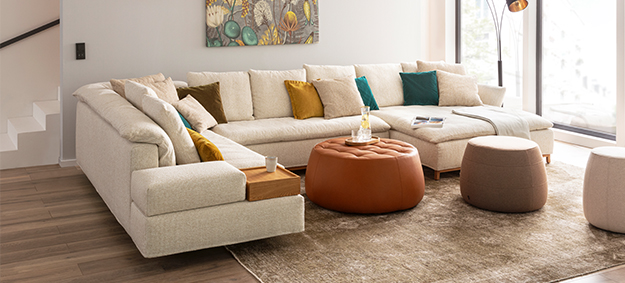 Modulares Ecksofa Isla von Signet mit Schlaffunktion, abgebildet in einem modernen Wohnzimmer mit dekorativen Hockern und Lederhocker.