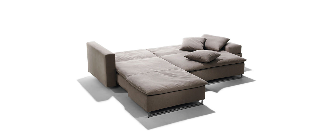 Ausgeklapptes Isla Ecksofa von Signet in braunem Stoff mit großzügiger Liegefläche und Edelstahlfüßen.